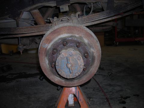 1995 Ford F-250 - Close-up view of a rusty rear axle hub and brake drum assembly supported by orange jack stands.