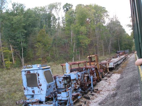 1998 Ford Crown Victoria - Derelict rail maintenance equipment rusting on a siding beside a wooded hillside: a faded light blue track machine with peeling paint in th…