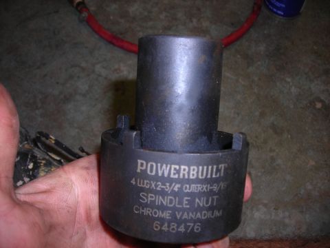 1995 Ford F-250 - A Powerbuilt spindle nut tool is held in a hand against a concrete background.