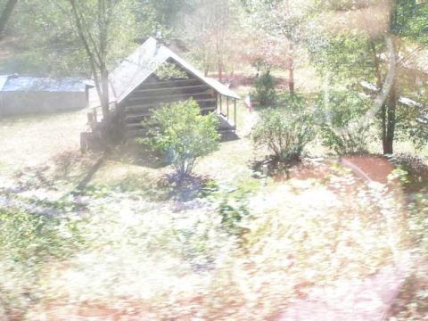 1998 Ford Crown Victoria - A badly overexposed, hazy shot of a small log cabin with a metal roof and covered porch set among trees, apparently taken through a window.…