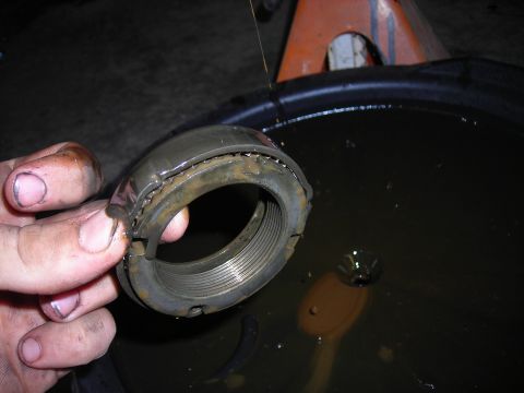 1995 Ford F-250 - A mechanic holds a damaged wheel bearing race, likely from a truck, over a pan of used oil.