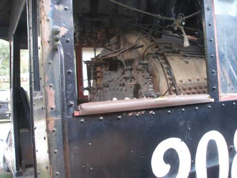 1998 Ford Crown Victoria - Close-up through the side cab window of a weathered steam locomotive, showing the riveted black cab sheet with white number lettering begin…