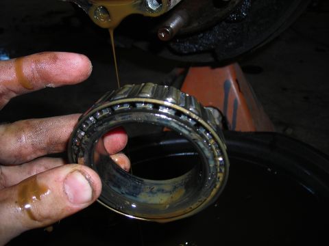 1995 Ford F-250 - A mechanic holds a greasy wheel bearing, with oil dripping from the vehicle's axle assembly.