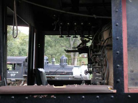1998 Ford Crown Victoria - Interior of a steam locomotive cab looking out the fireman's-side window, showing riveted black sheet steel, a row of overhead brass valve…