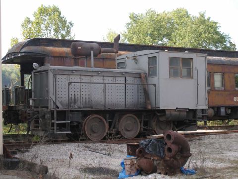 1998 Ford Crown Victoria - A weathered gray industrial switcher locomotive sits on rusty track at an outdoor rail museum, its louvered hood, exhaust stack and boxy ca…