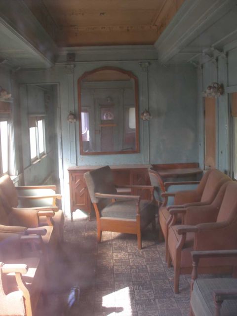 1998 Ford Crown Victoria - Interior of a vintage passenger rail car finished in faded pale-green paneled walls with a varnished wood ceiling, framed wall mirror, wall…