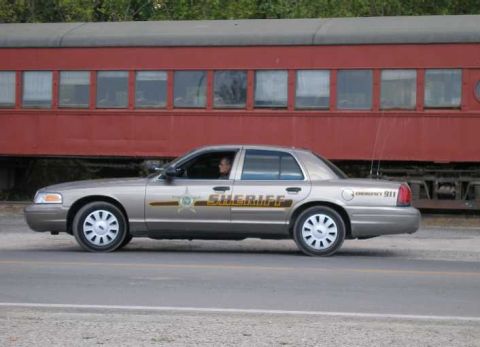 1998 Ford Crown Victoria - Tan/gold Ford Crown Victoria sheriff's cruiser in side profile with a gold star door emblem, 'SHERIFF' lettering and 'EMERGENCY 911' on the…