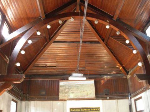 1998 Ford Crown Victoria - Interior ceiling of a wood-framed depot building, looking up at a varnished arched timber truss ringed with bare bulbs, tongue-and-groove p…