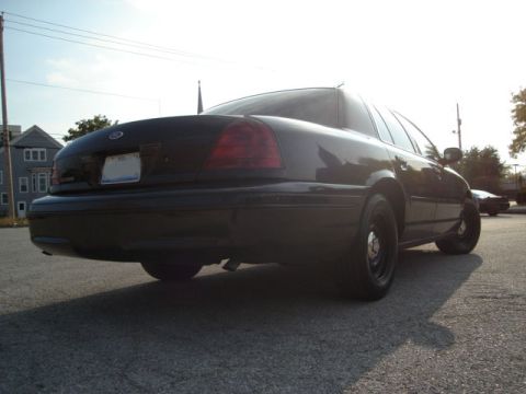 2000 Ford Crown Victoria - The rear of a black sedan is shown from a low angle on a sunny day.