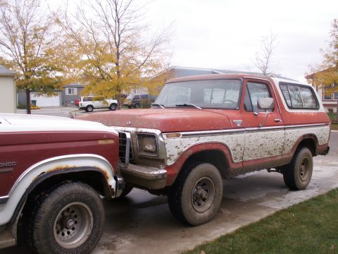 1984 Ford Bronco - A red and white Ford Bronco is parked on a driveway, showing signs of off-road use.