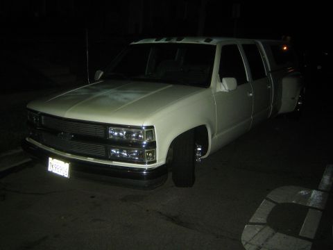 1990 Ford Bronco - white Chevrolet crew-cab dually pickup parked on a street at night, headlights on, with a billet grille and chrome bumper.