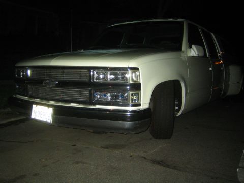 1990 Ford Bronco - Night front view of a white Chevrolet crew-cab dually pickup showing the bowtie emblem, billet grille and dual headlights.