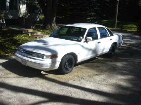 1997 Ford Crown Victoria - White 1997 Ford Crown Victoria sedan with black steel wheels parked on a concrete driveway.
