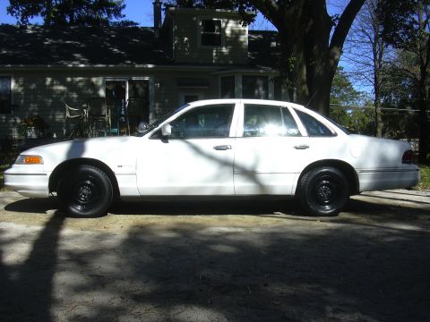 1997 Ford Crown Victoria - A white 1997 Ford Crown Victoria sedan is parked on a driveway in front of a house.