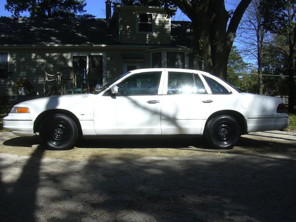 White 1997 Ford Crown Victoria sedan, side view, black steel wheels, parked on a driveway
