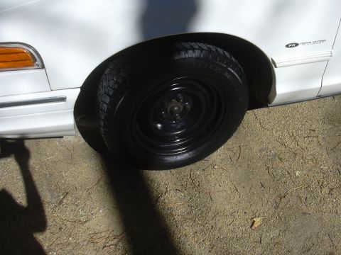 1997 Ford Crown Victoria - Close-up of the front fender and wheel of a white 1997 Ford Crown Victoria, showing a visible badge.