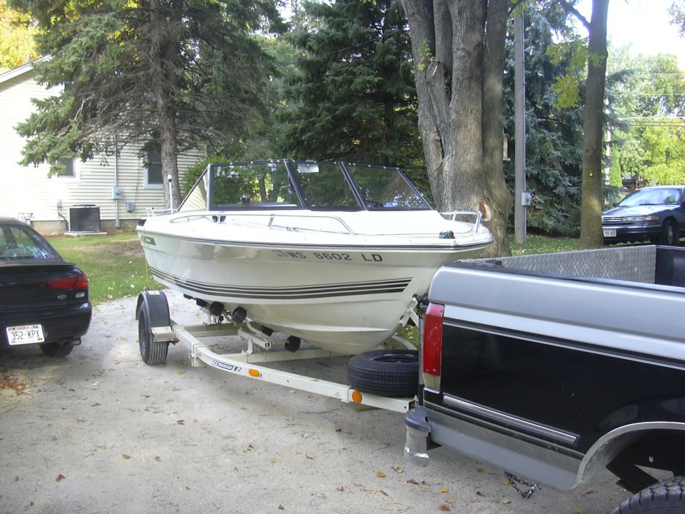 White runabout boat on trailer with reg WS 8602 LD, hitched to a dark pickup on gravel drive