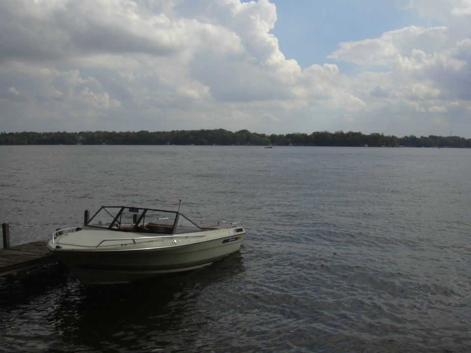 White runabout boat with tan interior docked at a wooden pier on a lake