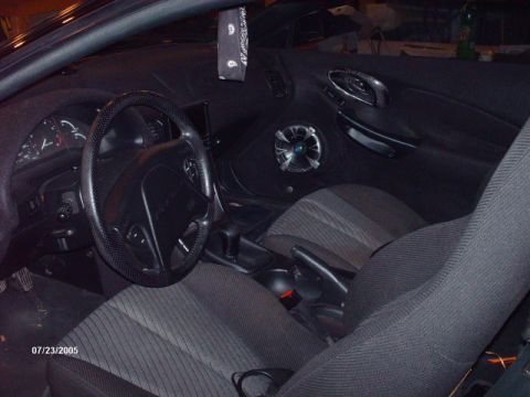 1995 Ford Probe - The interior of a car shows cloth seats, a speaker on the door panel, and a bandana hanging from the mirror.