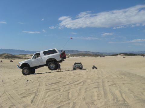 1994 Ford Bronco - Ford Bronco airborne during off-road dune activity with other vehicles present.