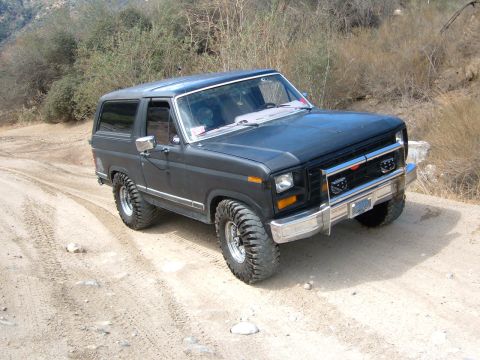 1981 Ford Bronco - This dark gray Ford Bronco is shown on a dirt road with off-road tires and a lifted suspension.