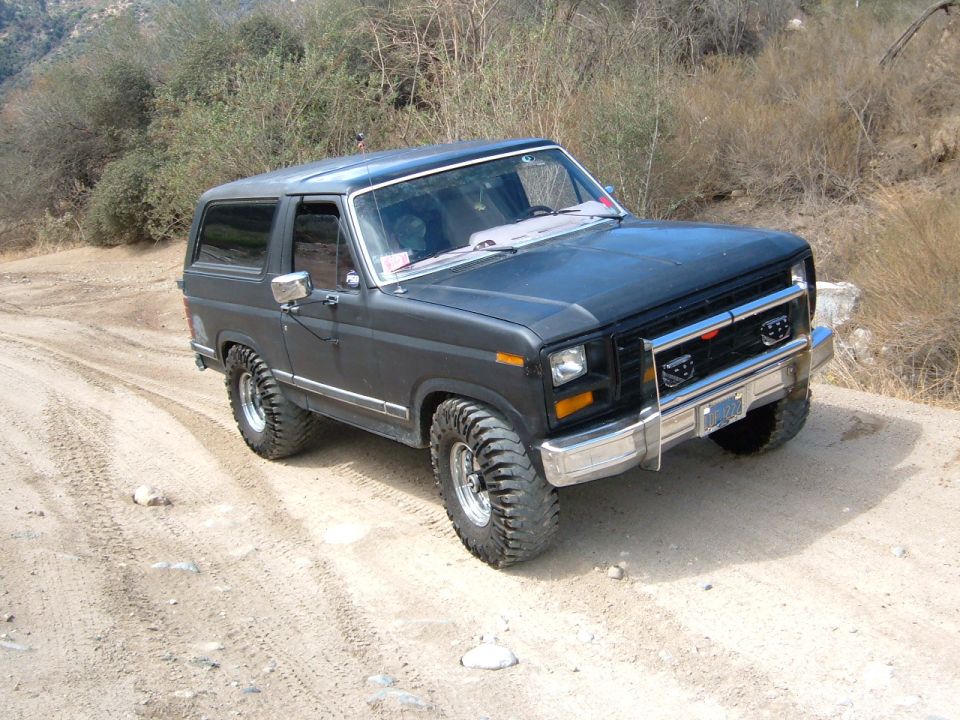 Dark gray Ford Bronco on a dirt road, lifted with off-road tires