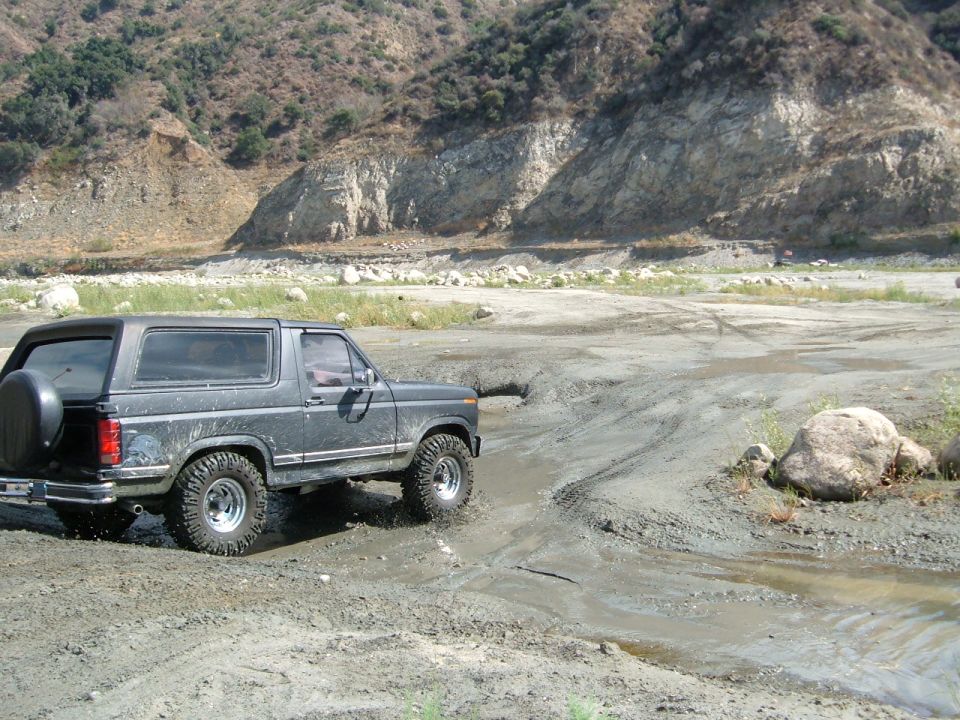 Dark gray Ford Bronco driving through mud, spare tire on rear door