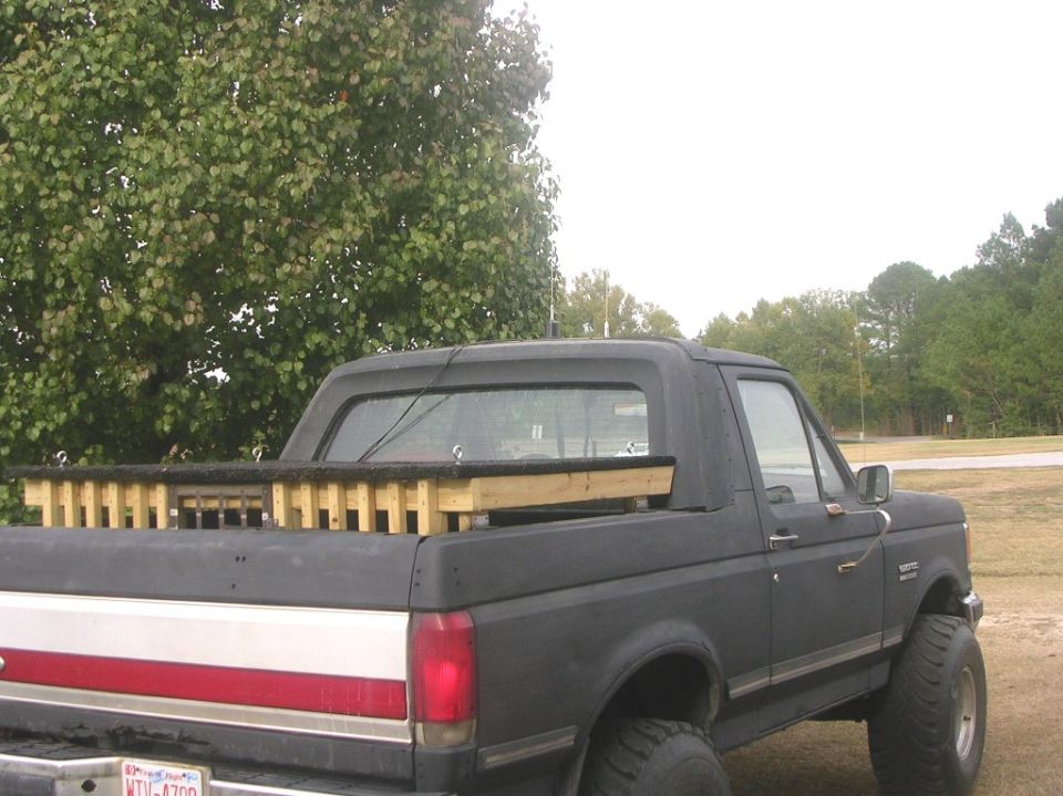 Black lifted Ford Bronco, rear 3/4 view, with wood bed rails and red/silver stripe.