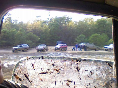 1989 Ford Bronco - Multiple off-road vehicles gathered in a muddy field with a wooded area behind them.