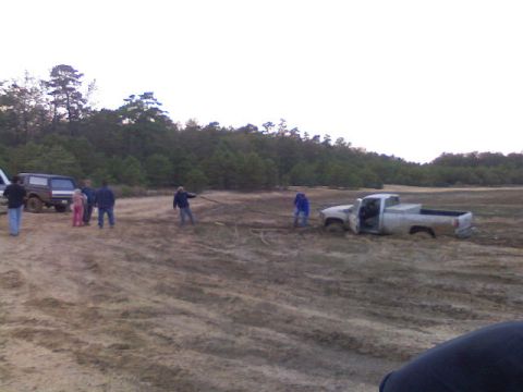 1989 Ford Bronco - A group of people are attempting to rescue a pickup truck stuck deep in the mud.