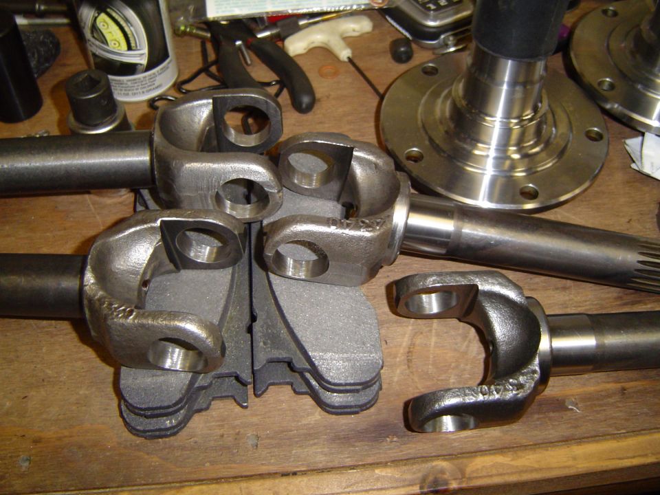 Forged 4x4 front axle shaft yokes and splined stub shaft with spindle laid out on a workbench