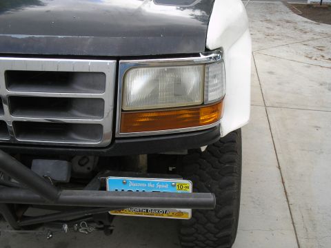 1990 Ford Bronco - Tight shot of the passenger-side front corner of a white Ford truck with a black hood protector, chrome-trimmed grille, and combination hea…