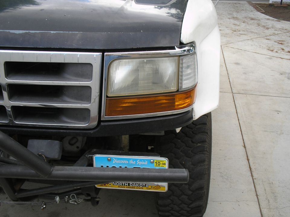 Front corner of white Ford truck: headlight, chrome grille, tube bumper, North Dakota plate