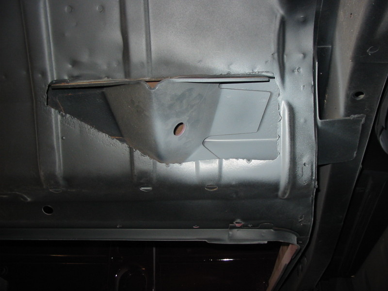 Gray-primered underbody floor pan with welded repair bracket in a rectangular opening