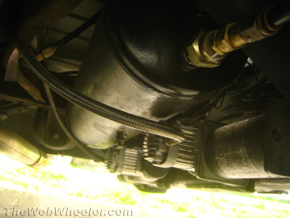 Black air tank and electric compressor with braided line mounted under a vehicle