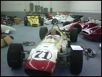 1965 Ford Mustang - A collection of open-wheel race cars are parked in a garage, with one car prominently the number 71.