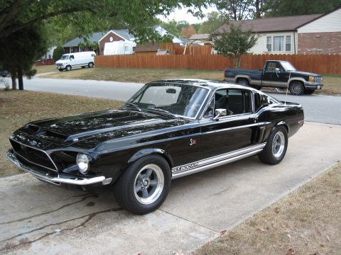 1968 Shelby GT500 - A classic black 1968 Shelby GT500 is parked on a concrete driveway in front of a residential home.