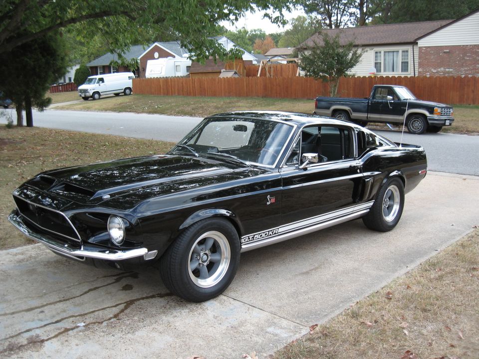 Black 1968 Shelby GT500 parked on a driveway, with a pickup truck and van in the background