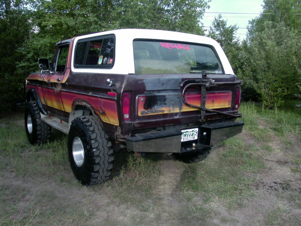 Rear 3/4 view of a 1978 Ford Bronco with a white top and multi-colored body, lifted with large tires