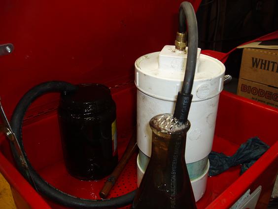 Red basin with a black fuel filter, a white canister, and a brown glass bottle collecting fluid