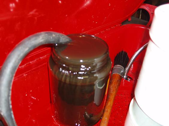 Jar of dark fluid next to a brush in a red container