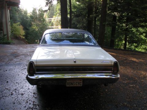 1972 Ford Ranchero - A vintage Mercury sedan is parked on a wet driveway surrounded by trees.