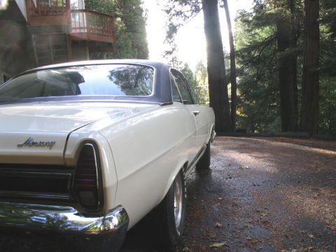 1972 Ford Ranchero - A white Mercury with a black vinyl roof is parked on a gravel driveway surrounded by trees.