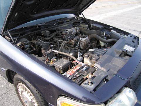 1991 Ford LTD Crown Victoria - The engine bay of a dark blue vehicle is shown with the hood raised.