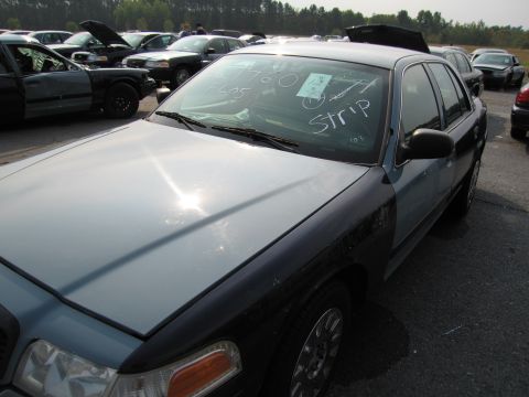 1991 Ford LTD Crown Victoria - A light blue and black Ford Crown Victoria is parked in a lot with other vehicles, and has writing on its windshield.