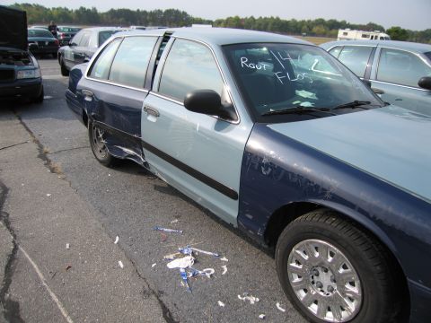 1991 Ford LTD Crown Victoria - A two-tone blue sedan with significant damage to its rear quarter panel sits in a lot with other vehicles.