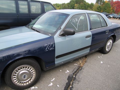 1991 Ford LTD Crown Victoria - Two-tone sedan with markings on the fender and window parked next to a van.