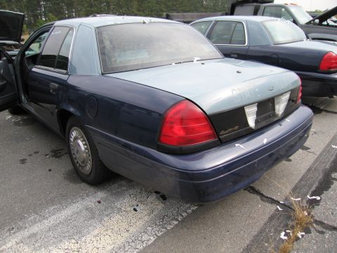 1991 Ford LTD Crown Victoria - Two Ford Crown Victorias are parked in a lot, one with its driver's door open.