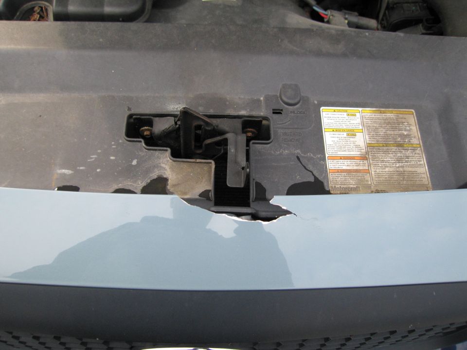 Engine bay latch mechanism with cracked plastic surround and warning labels