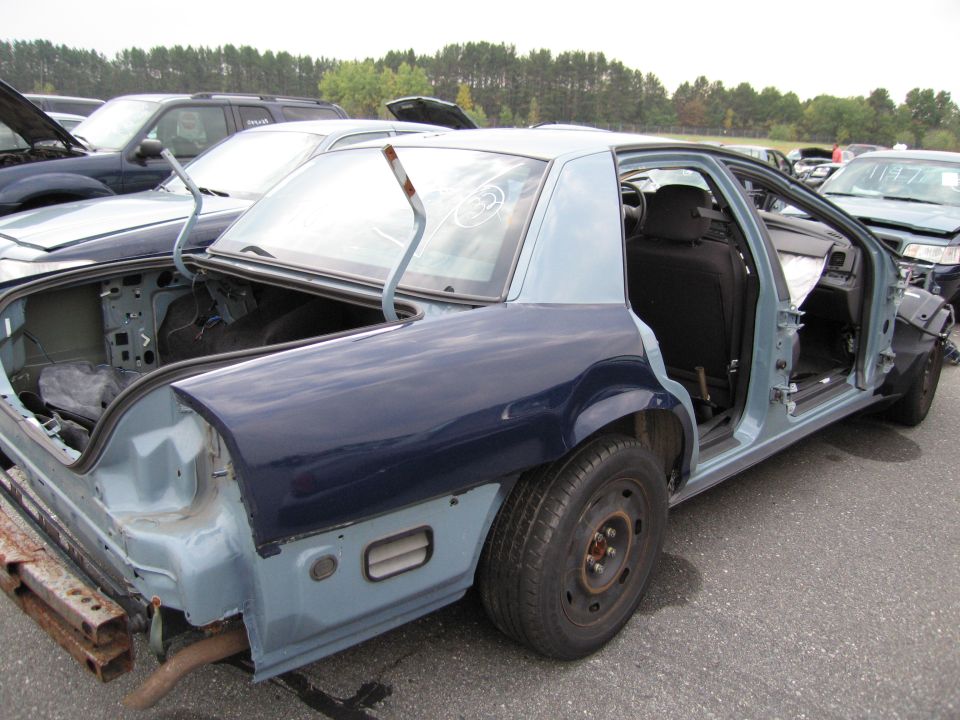 Damaged sedan with doors and trunk open, sitting in a junkyard lot